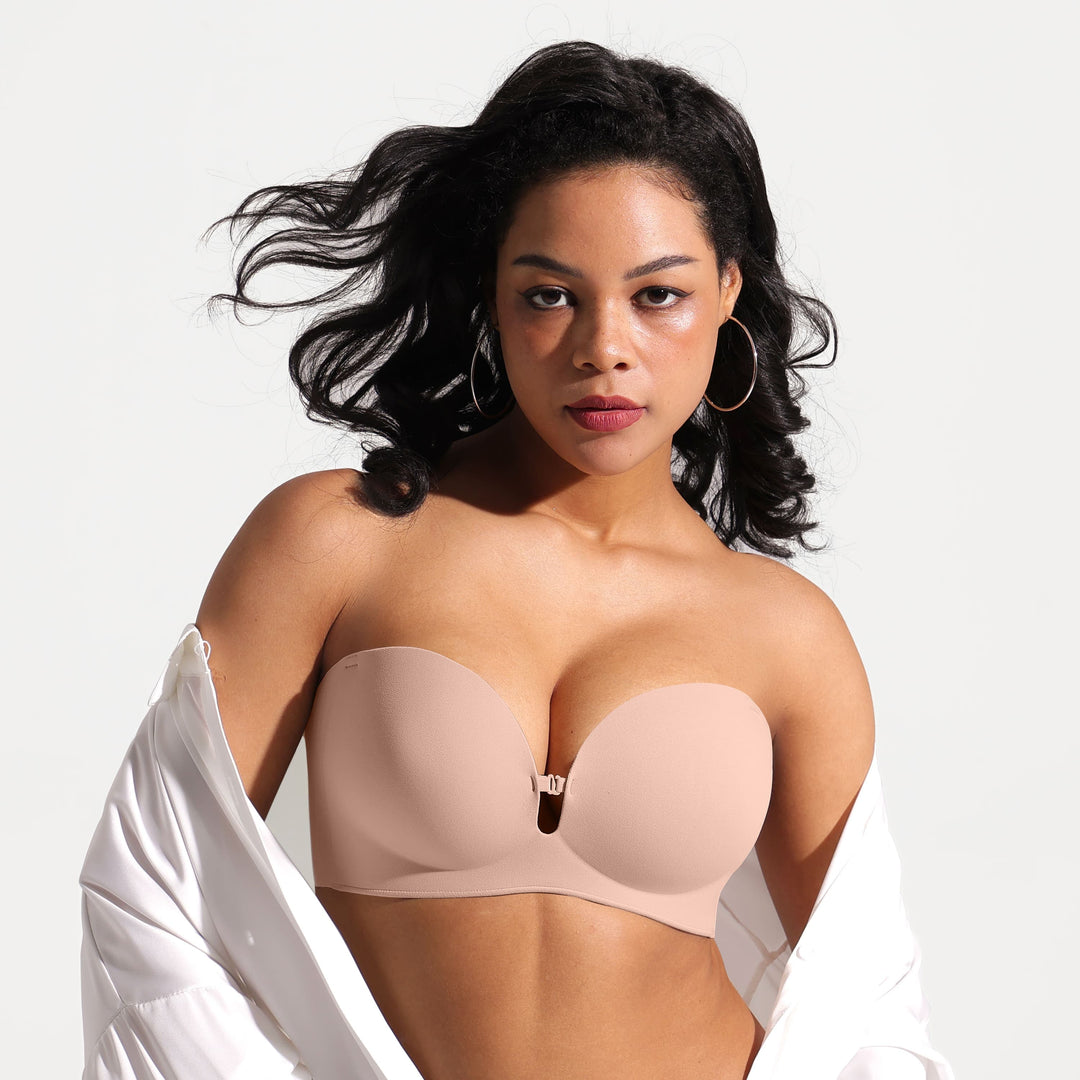Plus-size model wearing a light beige/nude strapless plunge bra with a front keyhole detail, paired with an open white shirt, against a plain white background